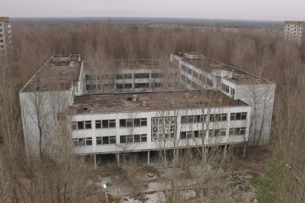 A natureza lentamente devora o concreto em Pripyat. Visto de cima, um prédio escolar abandonado revela árvores crescendo onde antes havia pátios e corredores, um retrato da cidade fantasma sendo engolida pela floresta.