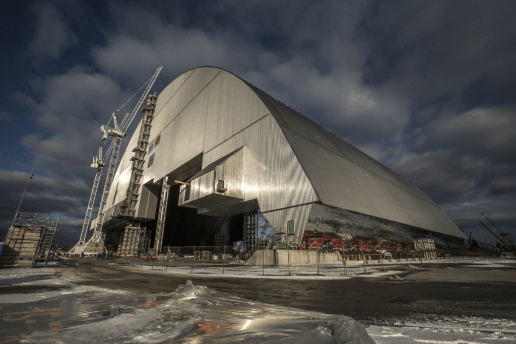 O Novo Confinamento Seguro: uma megaestrutura de aço que agora cobre o Reator 4. Este arco colossal, maior que a Estátua da Liberdade, é a tentativa da humanidade de conter o perigo radioativo por pelo menos um século.